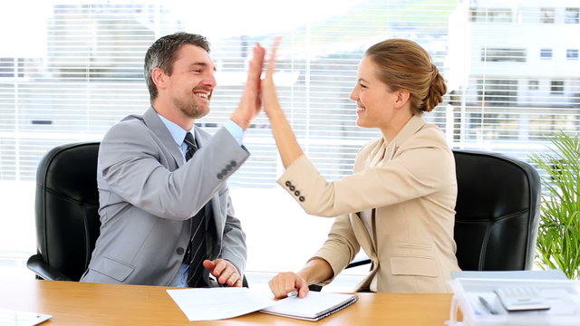 Business team looking at document and high fiving at desk
