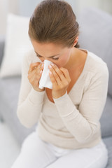 Young woman sitting on couch and blowing nose