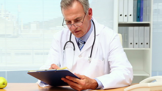 Doctor writing on clipboard at his desk