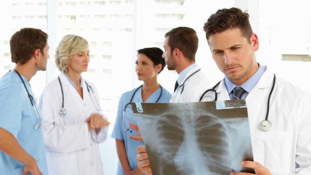 Serious doctor holding xray while staff are standing behind him