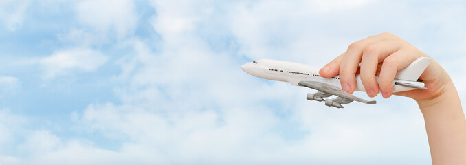 Child hand holding model airplane on sky background.