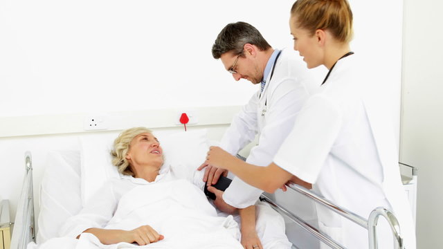 Doctors taking blood pressure of sick patient in bed