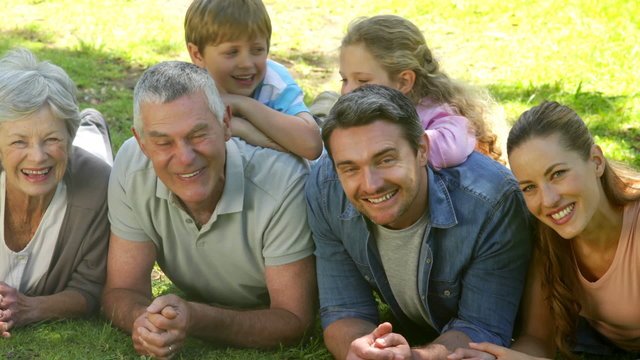 Multi generation family smiling and lying on ground in a park