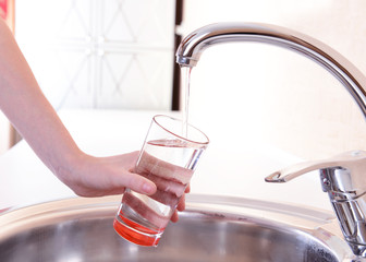 Hand holding  glass of water poured from  kitchen faucet