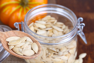 Pumpkin seeds in spoon and jar on table close up