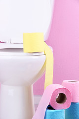White toilet bowl and colorful rolls of toilet paper, in