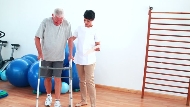 Smiling physiotherapist helping patient walk with walking frame