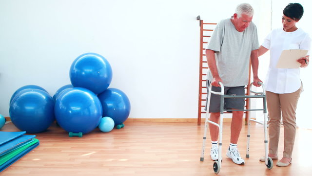 Smiling physiotherapist helping patient walk with zimmer frame