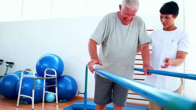 Smiling physiotherapist helping patient walk with parallel bars