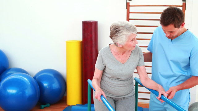 Physical therapist helping patient to walk with parallel bars