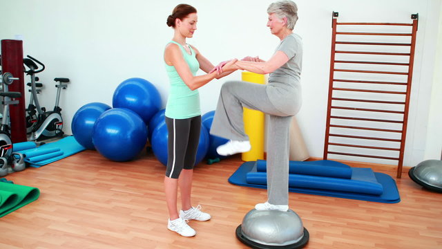 Trainer helping elderly client to use bosu ball