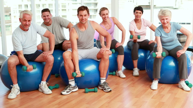 Fitness group sitting on exercise balls lifting hand weights