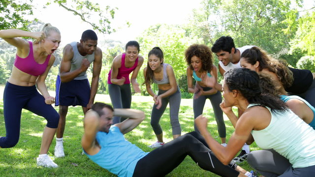 Fitness group cheering on man doing sit ups