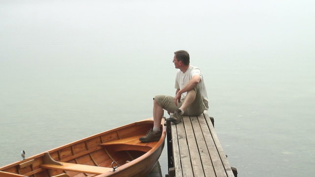 Mann sitzt auf Bootssteg an einem nebligen Herbstmorgen