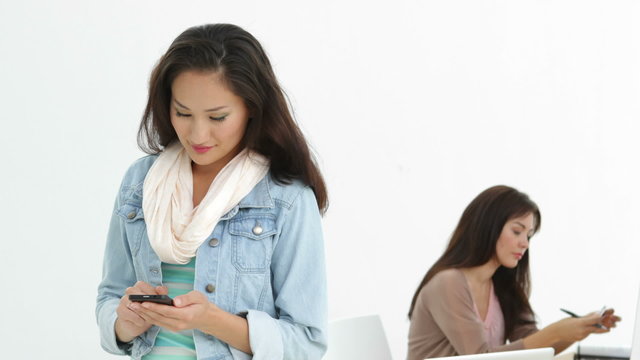 Creative businesswoman sending a text with coworker behind her
