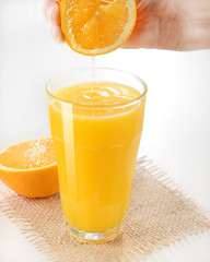 Hand squeezing a fresh orange on glass - Orange juice