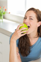 Smiling young woman eating apple in kitchen