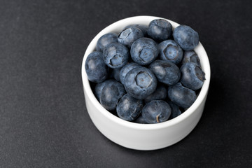 white bowl with blueberries on a black background, top view