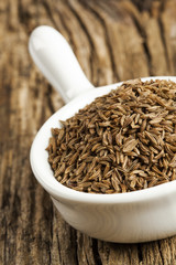 Cumin in white small bowl, old wood background