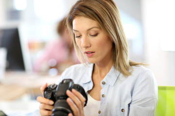 Woman reporter in office looking at photo camera