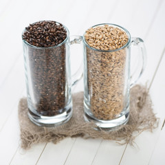 Two beer mugs with barley and hop over white wooden background
