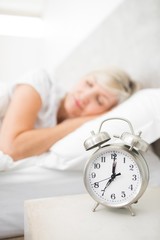 Woman sleeping in bed with alarm clock in foreground at bedroom