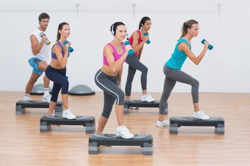 Fototapeta premium Fitness class performing step aerobics exercise with dumbbells