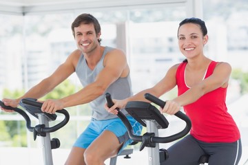 Fototapeta na wymiar Smiling young couple working out at spinning class