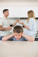 Obraz na płótnie Canvas Irritated boy covering ears while parents arguing