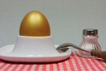 golden egg in an egg cup on a red patterned napkin