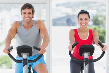 Smiling young couple working out at spinning class