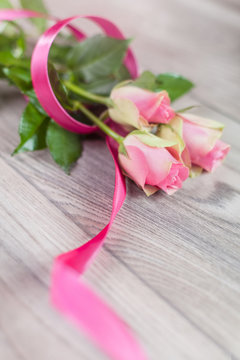 Pink roses with ribbon on wood