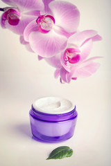 Obraz na płótnie Canvas Face/hand cream jar and purple orchid flowers, vertical shot