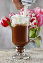Irish coffee on wooden table. Bouquet of pink and red tulips