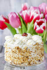 Round nut cake on cake stand. Beautiful bouquet of tulips