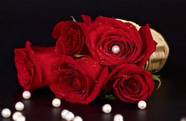 Red roses in a basket and white beads on a black background