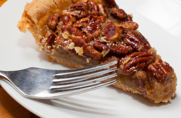 Rich dessert of pecan pie, a favorite for the holidays and gatherings with a fork next to it on the plate