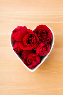 Red rose inside heart shape bowl on wooden background