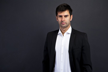 Young handsome man in black suit smiling on white background