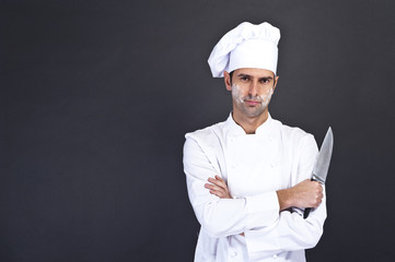Portrait of a young cook man wearing uniform holding a knife ove