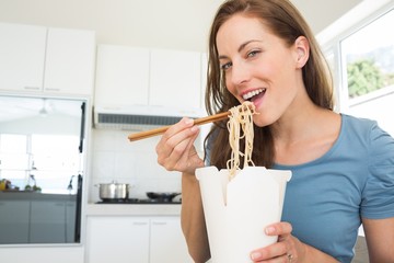Smiling young woman eating noodles in kitchen