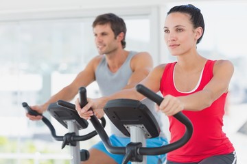 Fototapeta na wymiar Determined couple working out at spinning class in gym
