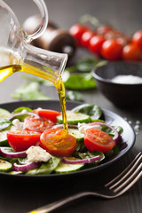 pouring olive oil on salad with tomato and cucumber