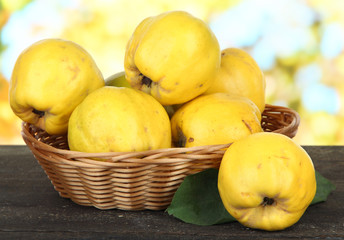 Sweet quinces in wicker basket on table on bright background