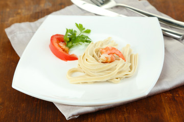 Pasta with shrimps on white plate, on wooden background