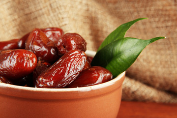 Dried dates in bowl on table on sackcloth background