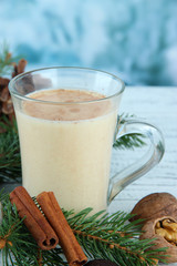 Cup of eggnog with fir branches on table on bright background