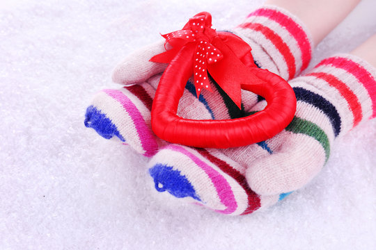 Female hands in mittens with heart on snow background
