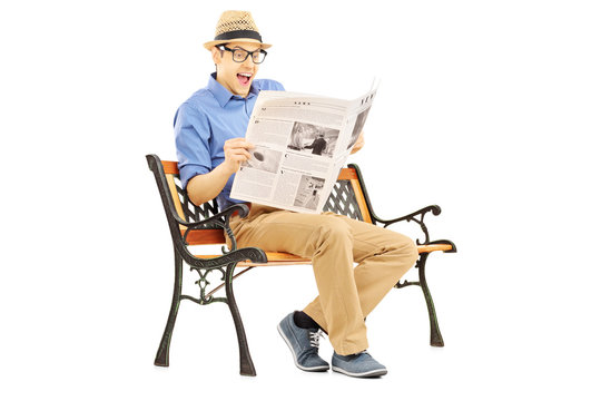 Surprised young man reading the news seated on a bench