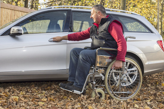 Man in a wheelchair in the fall next to their car